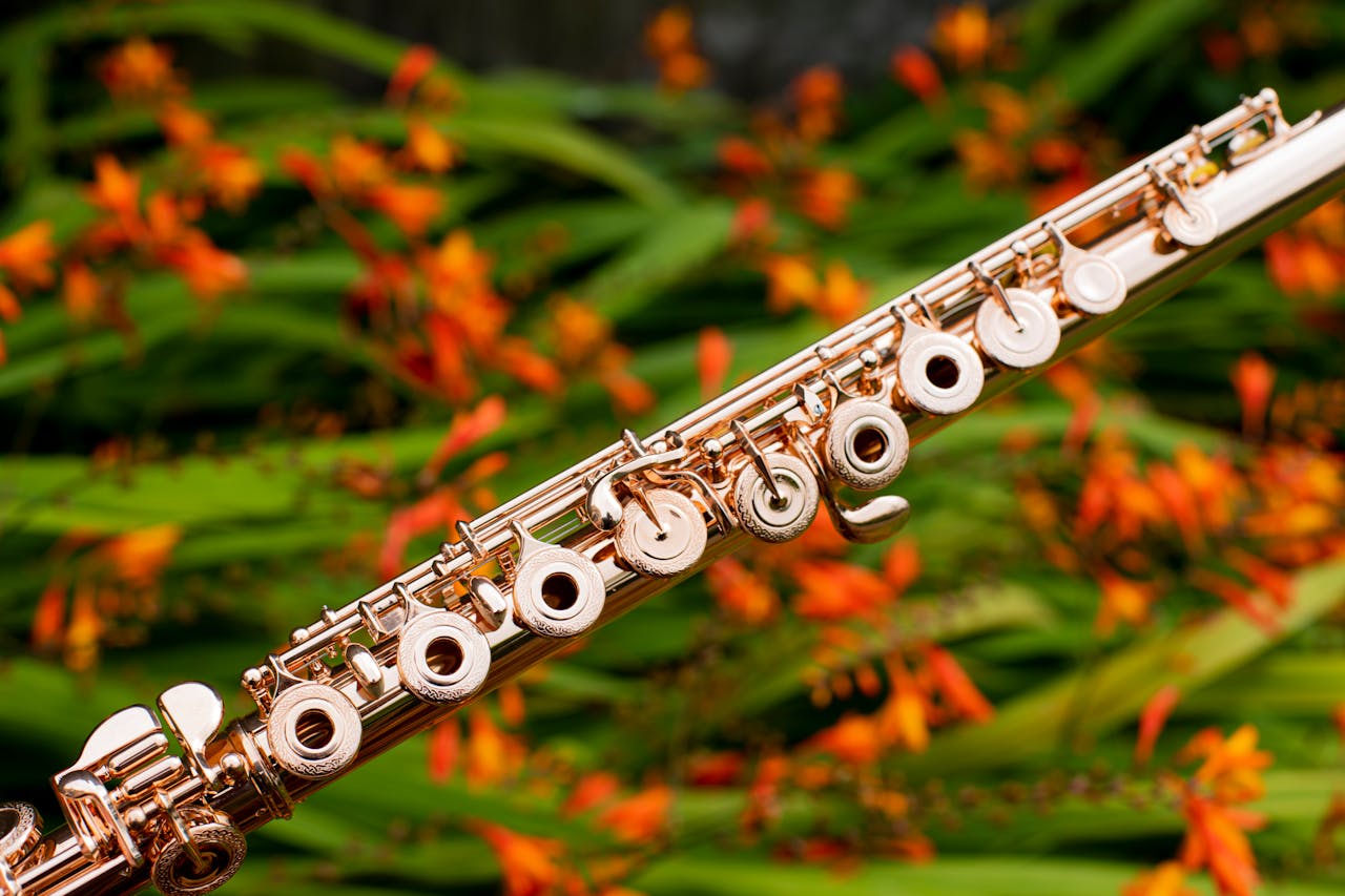 Close-up of a gold flute with vibrant orange flowers as the background, showcasing a blend of music and nature.